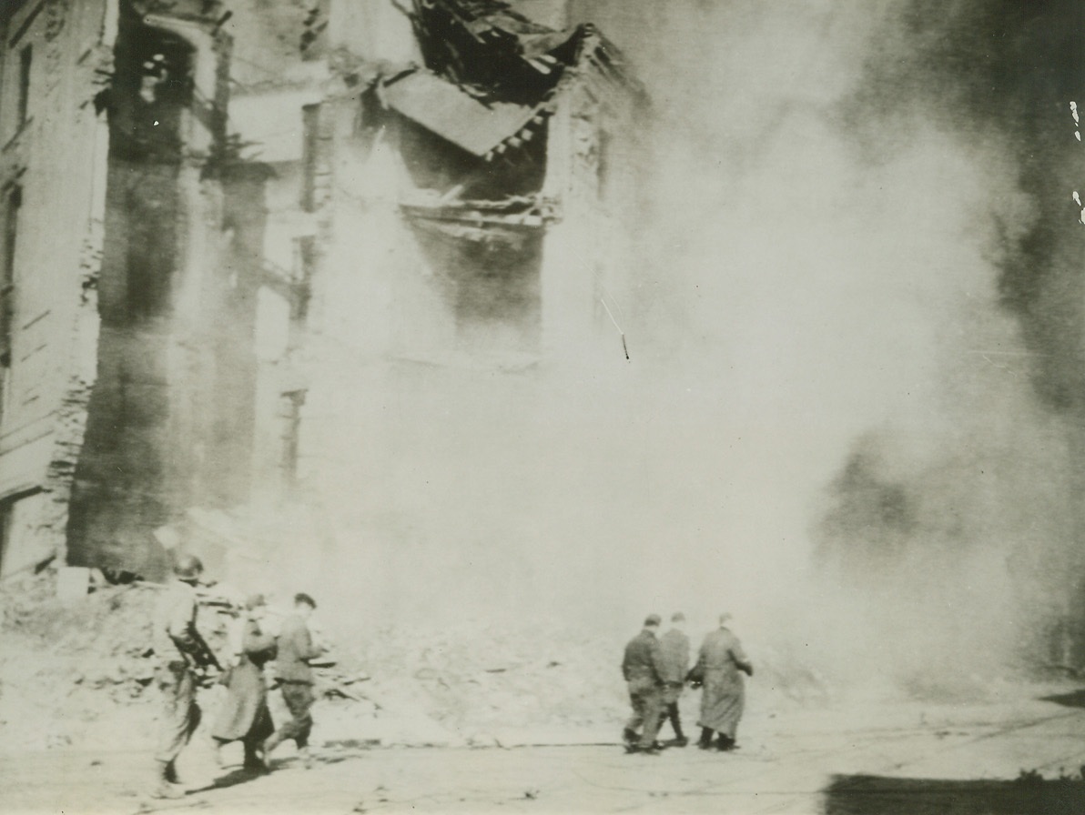AACHEN BATTLE SCENE, 10/17/1944. GERMANY—Smoke from blazing buildings, wrecked masonry and smashed concrete form a Mars-like background for an American soldier as he escorts five Germans at gunpoint through the city of Aachen to prison compounds.Credit: Photo by Acme Newspictures photographer, Bert Brandt, for the War Picture Pool;