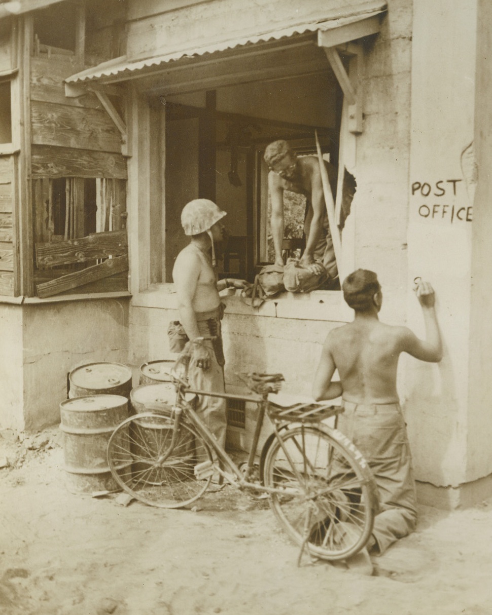 P.O. but no O.P.A., 7/3/1944. Saipan – Marine Postal Clerks set up a post office in a vacant Jap building on Saipan. Office is complete to the painted shingle. One of the Leathernecks commandeered a Jap bicycle but the rubber situation being what it is, couldn’t get a front tire for the vehicle. Credit: Marine Corps Photo from ACME;