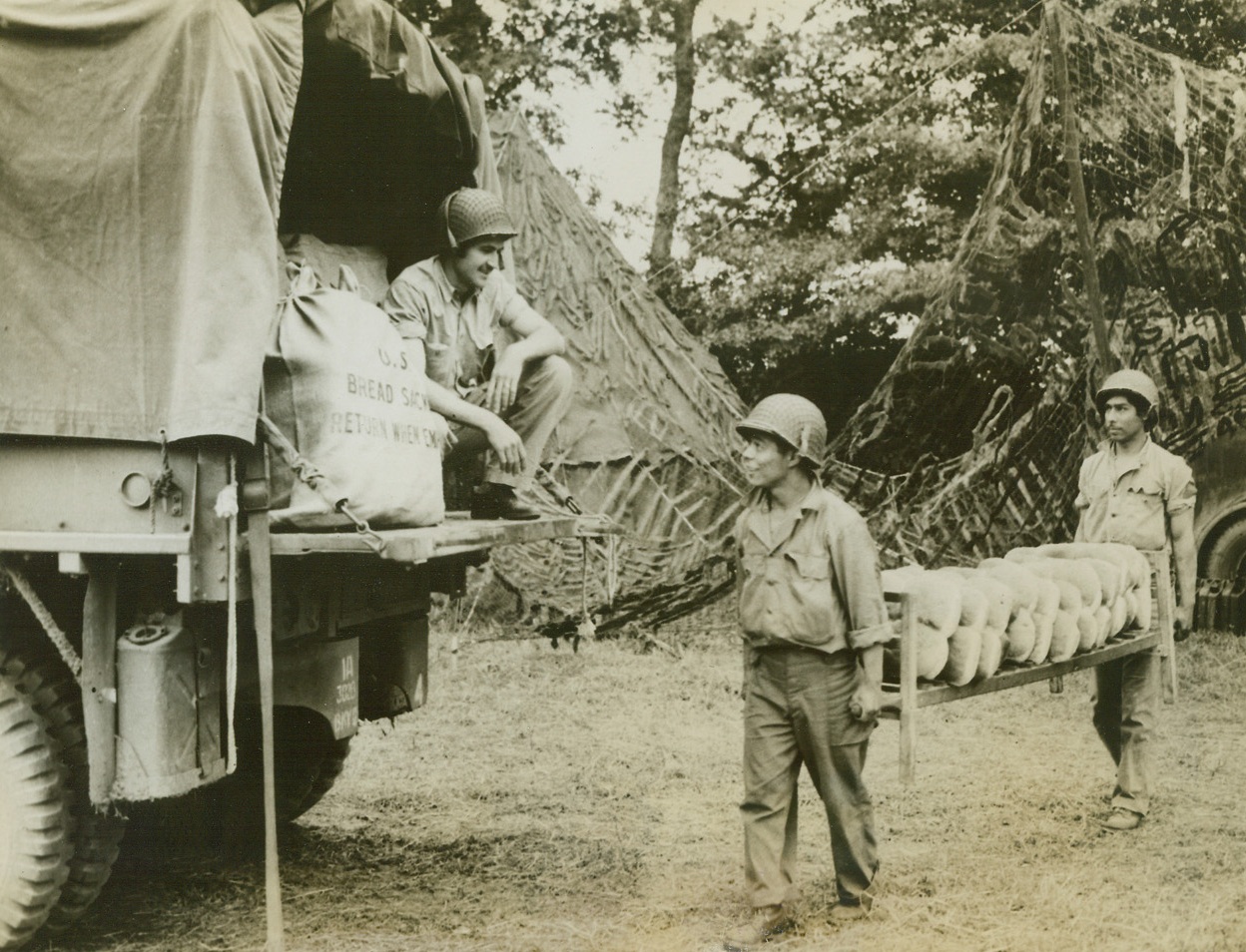 Here’s Bread For The Fighters, 7/17/1944. Somewhere in France – Beginning delivery of the Staff of Life to Yanks fighting on the Normandy front, these Texans load fresh loaves of bread on an Army truck. Pvt. Garth Gilbert of Huntington, Tex., squats on the truck as Cpl. Antonio Palacio of El Paso, and Cpl. Manuel Ricondo (in rear) of San Antonio, bring up the loaves. Credit: ACME;