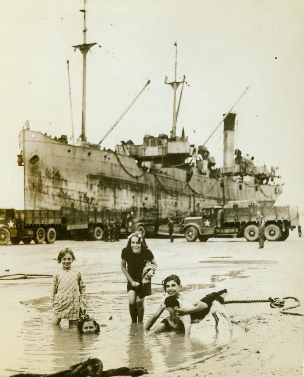 French Children Frolic Near Invasion Craft, 7/28/1944. France -- French children wade in a pool on the beach at Arromanches in the shadow of an invasion craft unloading its cargo Fun has reentered the lives of the children of France in the liberated coastal areas of Normandy. 7/28/44 (ACME);