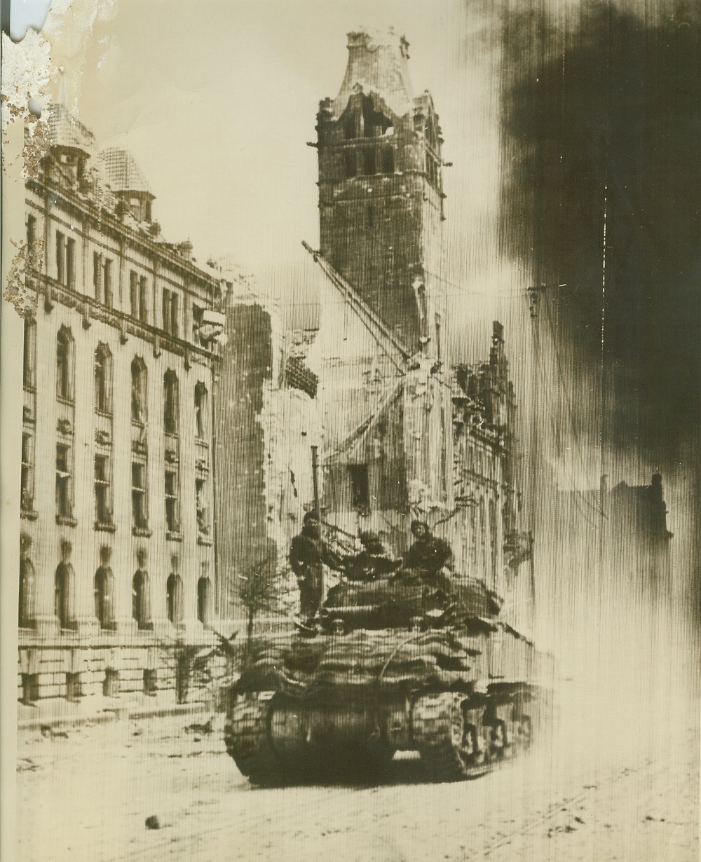 Yanks in Magdeburg, 4/18/1945. GERMANY – A tank of the 2nd Armored (Hell on Wheels) Division of the U.S. 9th Army, rumbles through a street in Magdeburg, against a backdrop of smoke and flames from still burning buildings. Ruins of the buildings show effects of the terrific battle of the city. Credit: (U.S. Signal Corps Radiophoto from ACME);