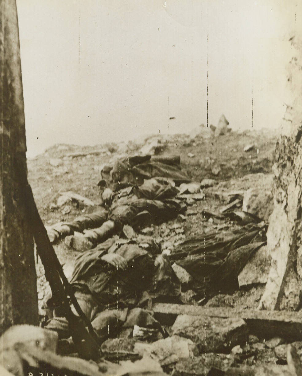 Death Plays No Favorites, 12/13/1943. ITALY – Death favors no side in this war. Dead British and German soldiers lay side by side before the jagged entrance to Monastery Hill, where in life they fought each other hand to hand, with ‘no quarter” hostilityCredit (Signal Corps Radiotelephoto from Acme);