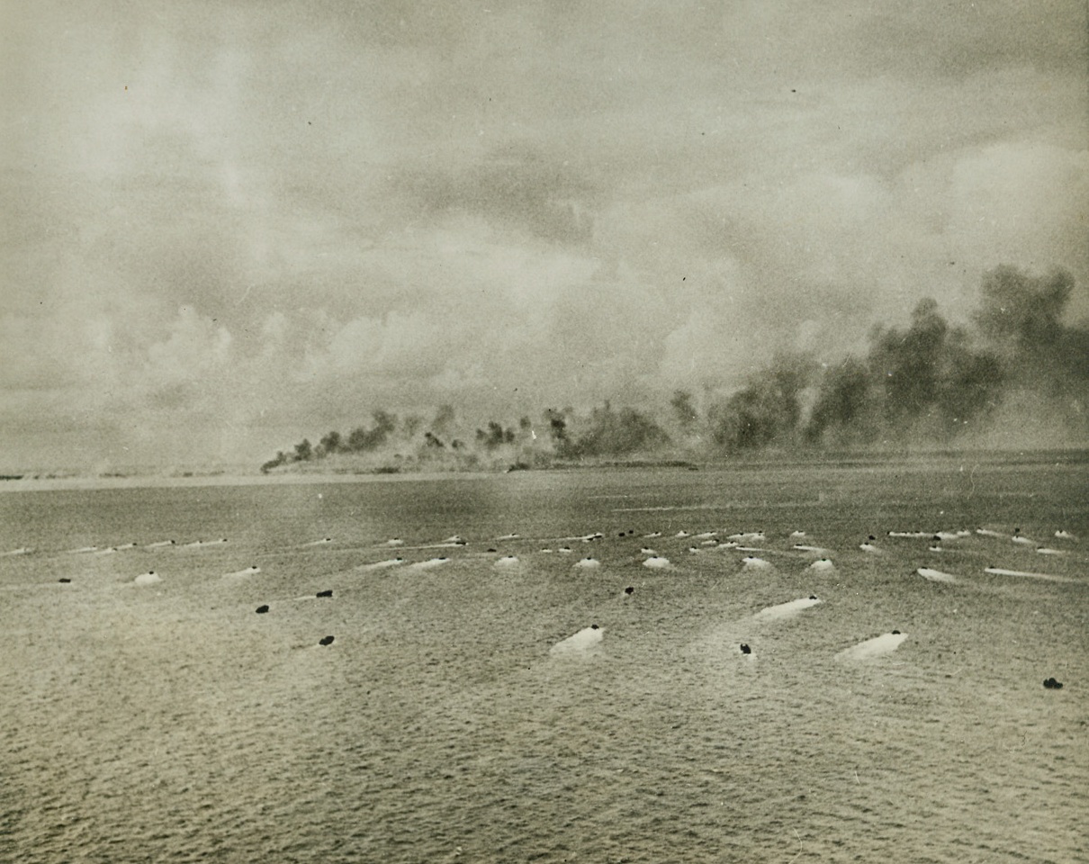 During Battle at Tarawa, 12/16/1943. This photo, taken from the air during the battle for Tarawa, shows landing craft streaking for the shore loaded with U.S. troops, while in the background columns of smoke mark an island of the Tarawa group under heavy bombardment by Allied Air and Sea Forces. The battle was the bloodiest in the history of the U.S. Marine Corps, and both Japs and Americans lost heavily. (Passed by Censors) Credit: ACME