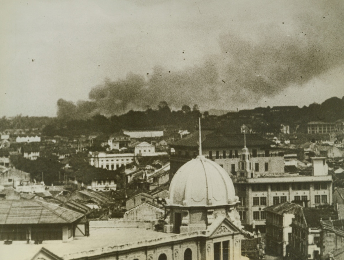 SMOKE HOVERS OVER DOOMED SINGAPORE, 3/8/1942. SINGAPORE, MALAYA—Blasted by bombs and artillery fire, doomed Singapore huddles beneath a dense pall of smoke shortly before its capture by the Japanese. Credit: Acme;