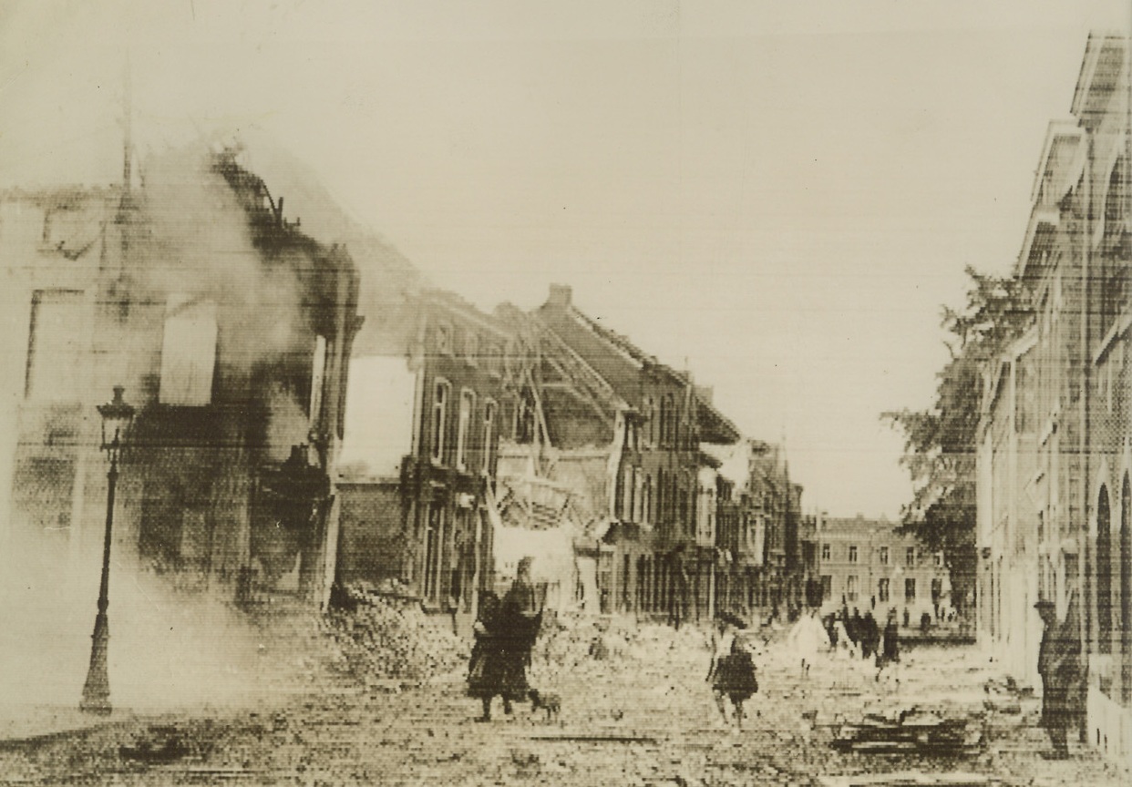 Remains of Louvain, 5/18/1940  LOUVAIN, BELGIUM—Remaining inhabitants of Louvain, Belgian town which was devastated during the World War and rebuilt largely with American funds, pick their way over heaps of debris lying in the street and past houses gutted and shattered by Nazi bombs in the 1940 invasion. The photo rushed to London, whence it was transmitted to New York via cable. Credit: ACME.;