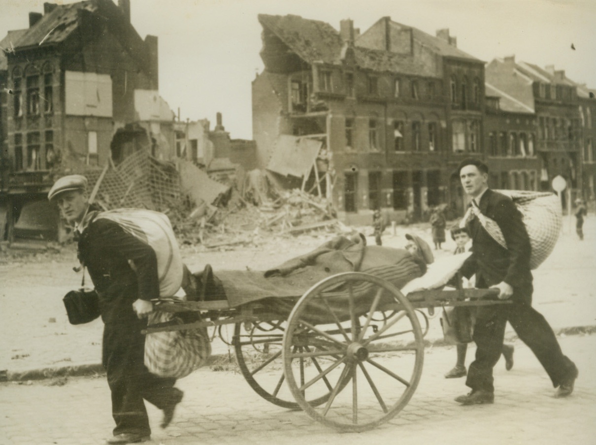Rolling to Safety, 5/27/1940  LOUVAIN, BELGIUM – A push cart serving as a rolling stretcher for an invalid man being wheeled to safety by a pair of younger and more fortunate men. The scene is in Louvain, Belgium, where some of the extensive bomb wreckage is plainly seen.Credit: (ACME);
