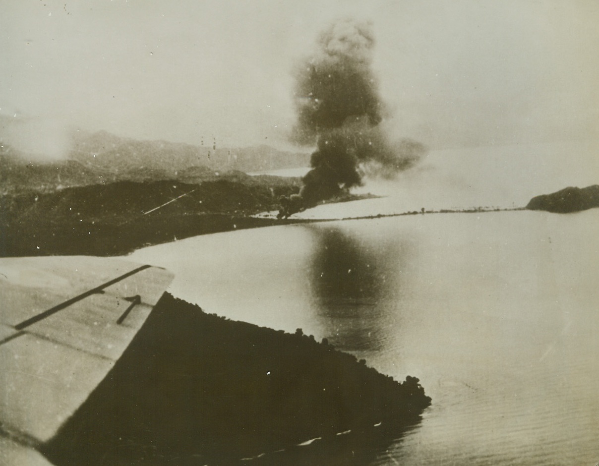Allies Attack Salamaua, 5/20/1943. This photo, released in Washington today, shows smoke rising from fires set by Allied bombs on the Jap-held base at Salamaus, New Guinea, recently.  A wing of one of the bombers making the raid shows at lower, left (photo above).  It was announced today that allied planes had again raided Salamaua, attacking the airdome and town area and starting fires in enemy installations along the Francisco River.Credit Line (U.S. Army Air Forces photo from ACME);