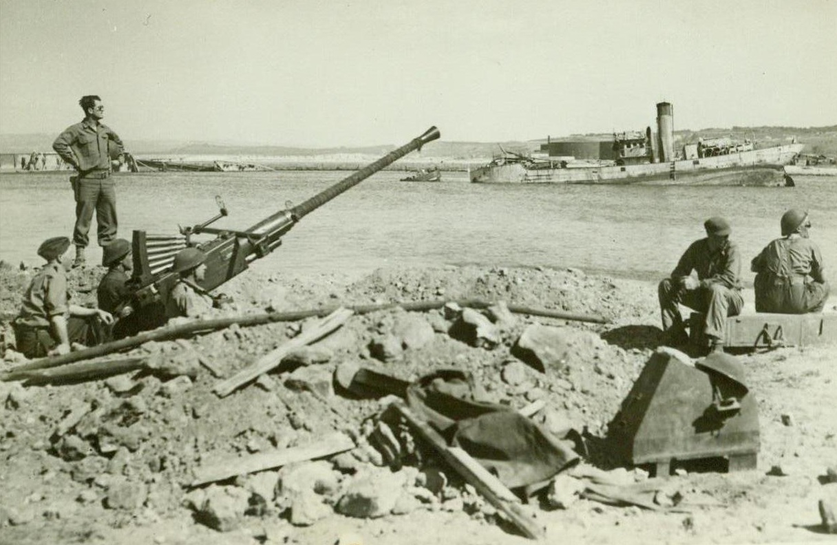 On the Alert in Bizerte, 5/24/1943. BIZERTE, TUNISIA - As the Germans were...swept from Tunisia, the crew of a United...anti-aircraft gun maintain watch for...planes from a foxhole emplacement at...The hulk of a ship resting on bottom...harbor can be seen in the background...;