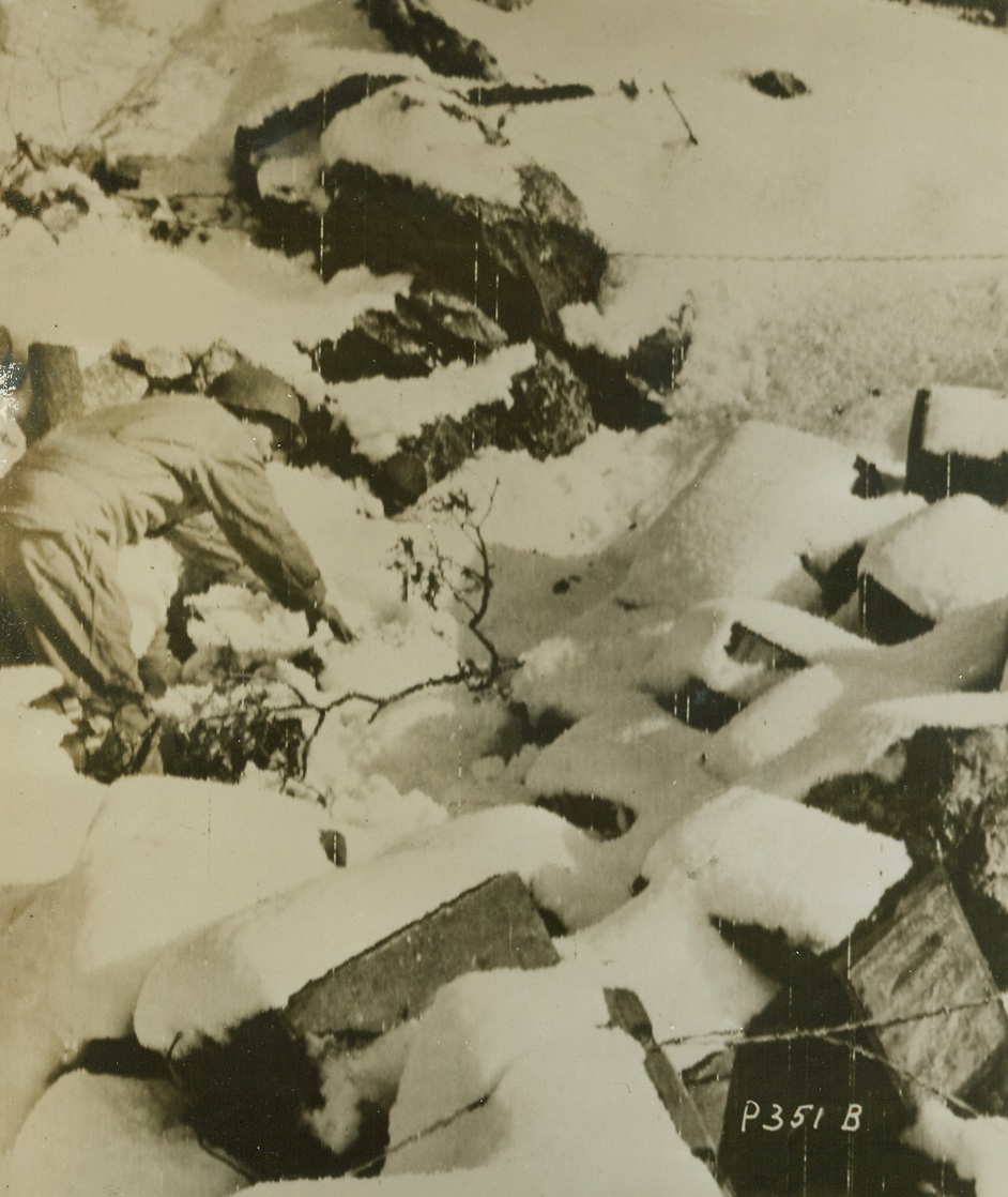 Camouflage, 1/6/1944. SOMEWHERE IN ITALY—Heavy snowfall provides camouflage at the Italian front as Pfc. Charles P. Nelson of Caldwell, N.J. brushes snow from shells in a dump in Pozzili area. Credit: SIGNAL CORPS RADIOTELEPHOTO from ACME.;