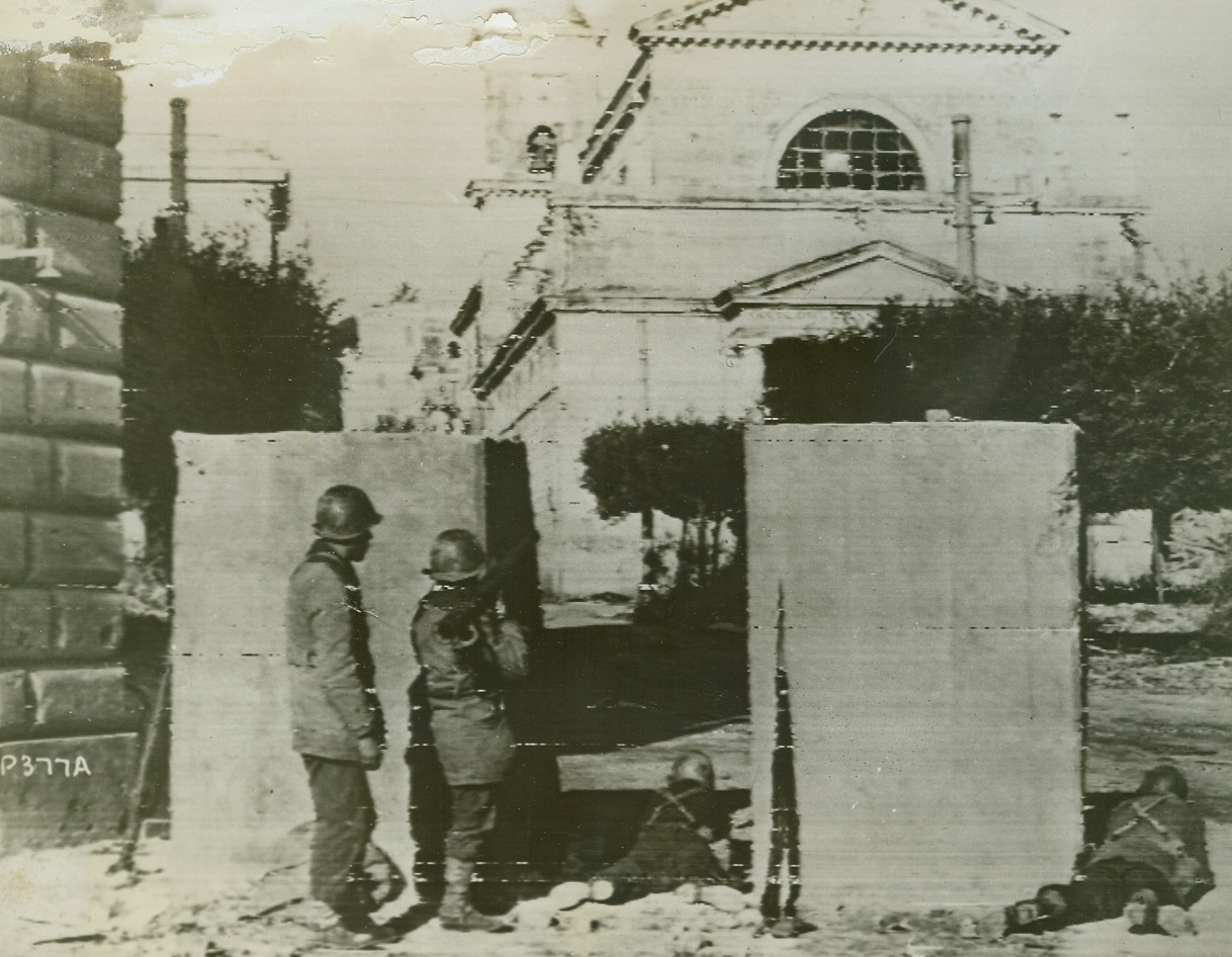 CONCRETE SHELTER, 1/27/1944. ANZIO, ITALY—Retreating Germans erected these concrete blocks to tie up roads in Anzio, but they served the American troops well as our fighters entered the town. The blocks provided cover for Yanks firing on the Nazis. At right, one soldier mans a bazooka gun. Credit: U.S. Signal Corps radiotelephoto from Acme;