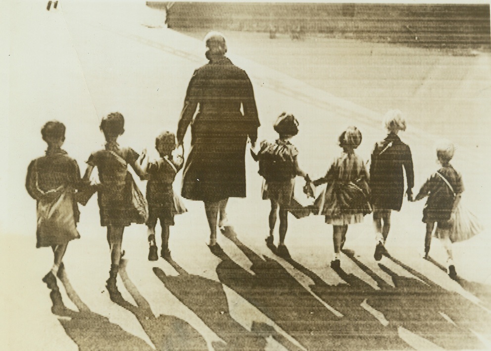 London Children Mobilized for Evacuation, 8/28/1939. LONDON – London school children, emergency kits strapped to their backs, being mobilized for evacuation of the city. As this photo was cabled to New York, Aug. 28, arrangements were perfected for a poignant war rehearsal—the practice by school children all over Great Britain of the plan worked out for them to leave their homes in event of an air alarm, go to their schools, and accompany their teacher, as shown above, to previously designated refuges in the countryside. Credit: (ACME Cablephoto);
