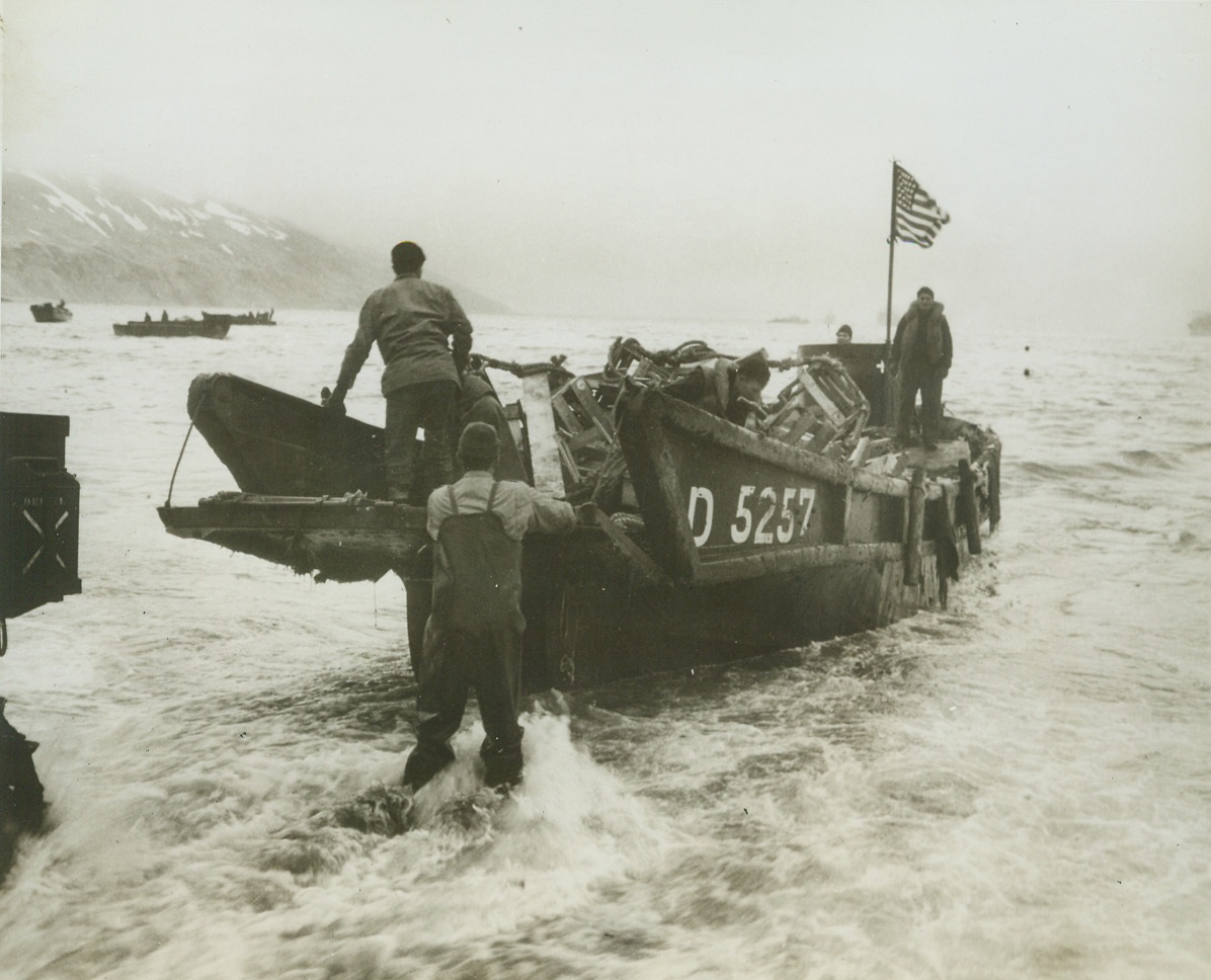 “Old Glory” Takes Possession,  5/27/1943. Attu – The American flag flutters from a mast in this captured Jap landing boat as our men bring it ashore on the beach of Attu’s Massacre Bay.  Latest reports from that Aleutian Island indicate that fierce hand-to-hand fighting is now under way in the primitive wilds of Attu, with U.S. troops believed to be hacking their way through death traps with bayonet and grenade.Credit Line (Official U.S. Navy photo from ACME);