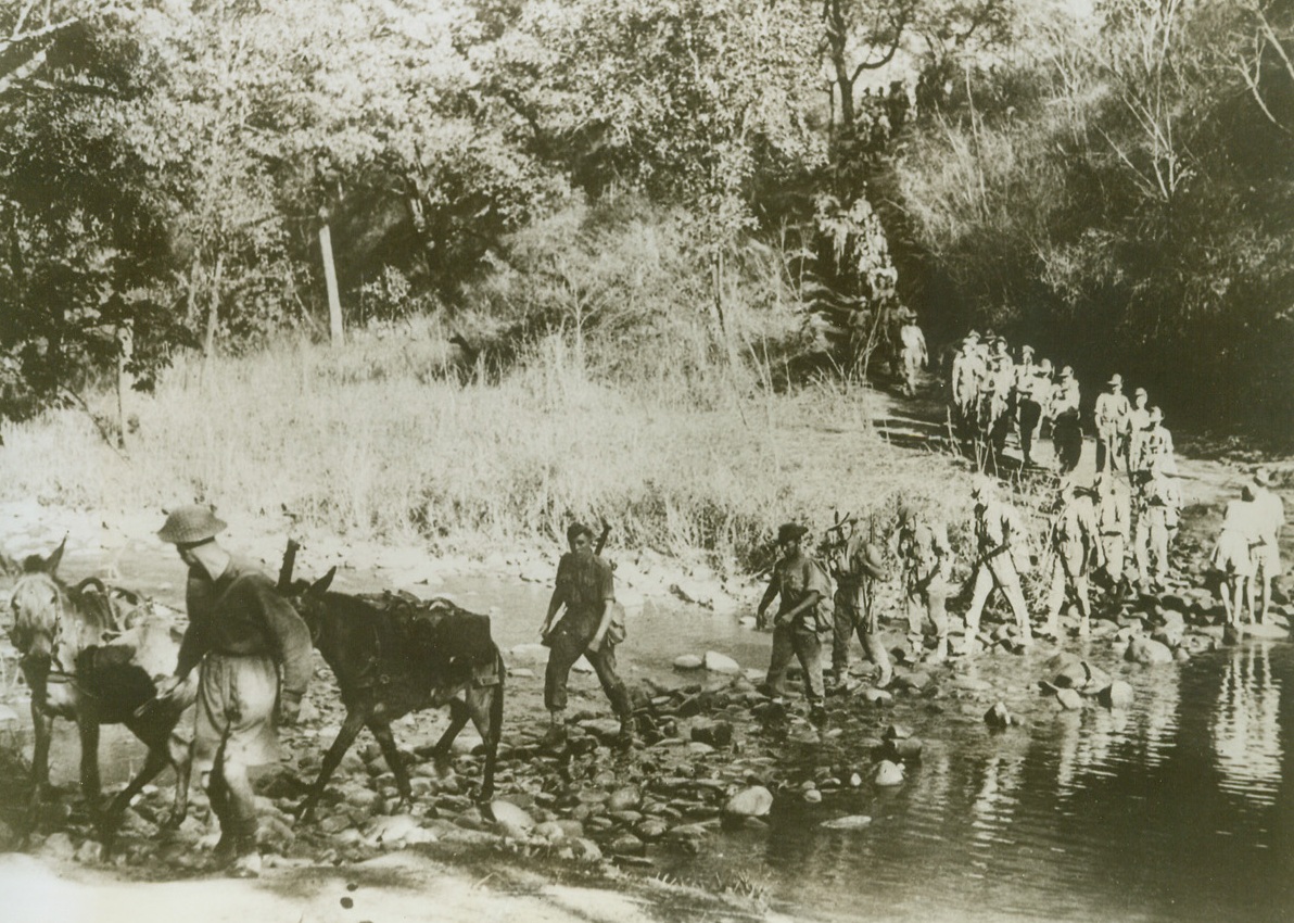 STEPPING STONES TO BURMA, 5/21/1943. BURMA—Stepping stones help Allied soldiers and their supply mules to cross this jungle stream on the narrow road to Burma. Cut through jungle, forests and mountains; this road must serve as a supply route for the Allies until the Japs can be chased from Burma and the Burma Road reopened. The key to China, which must be given military aid before a successful attack on the Japanese empire can be launched, Burma is probably the center of attention in long-range Pacific strategy discussions now being held in Washington.  Credit: ACME.;