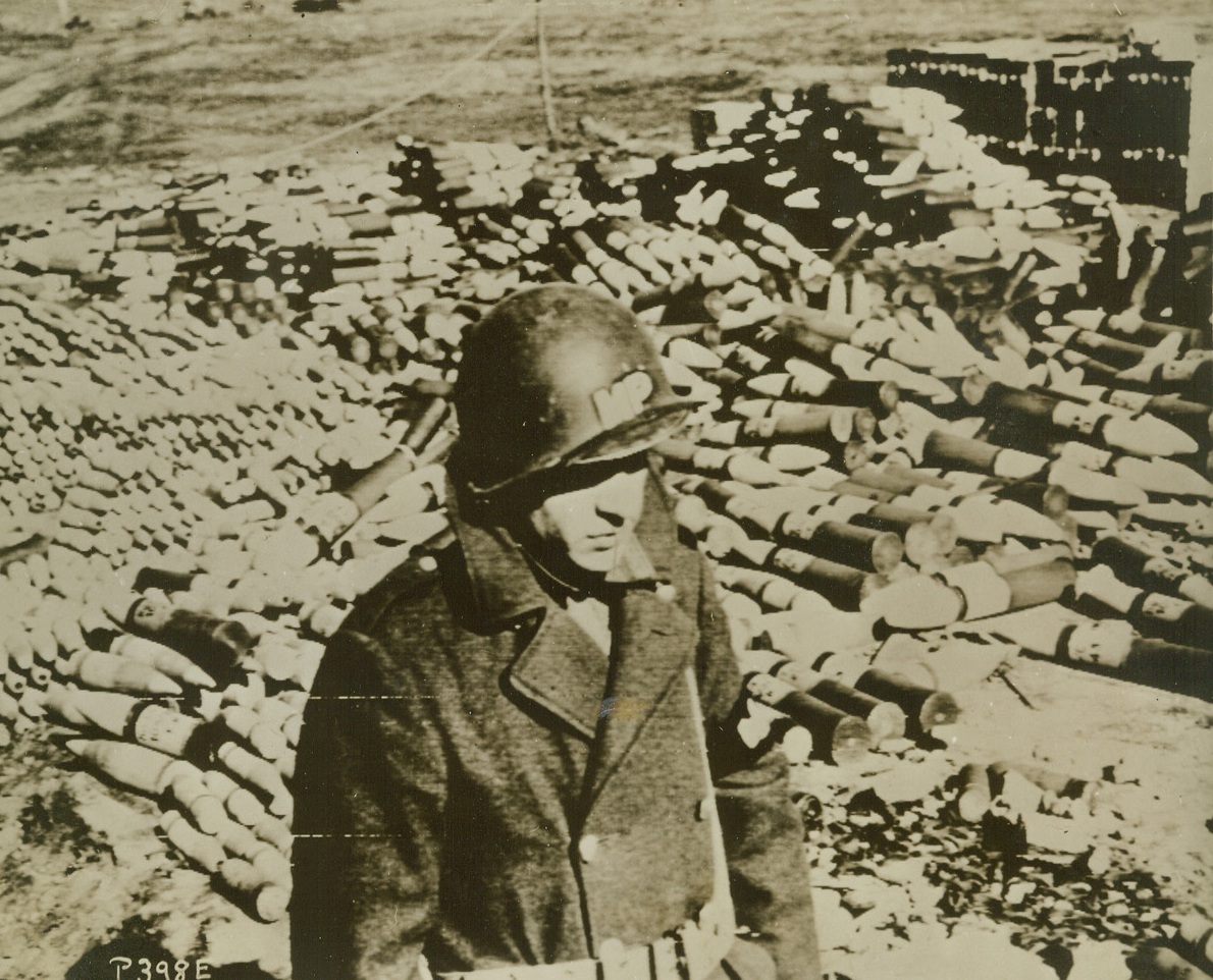 CAPTURED NAZI BOOTY, 2/13/1944. ITALY—A field chock-full of captured German ammunition and mines is guarded by Pfc. Michael Paulik, MP from Pittsburgh, Pa., who is fighting in the Nettuno beachhead area. Credit: Acme photo by Bert Brandt via Army Radiotelephoto;