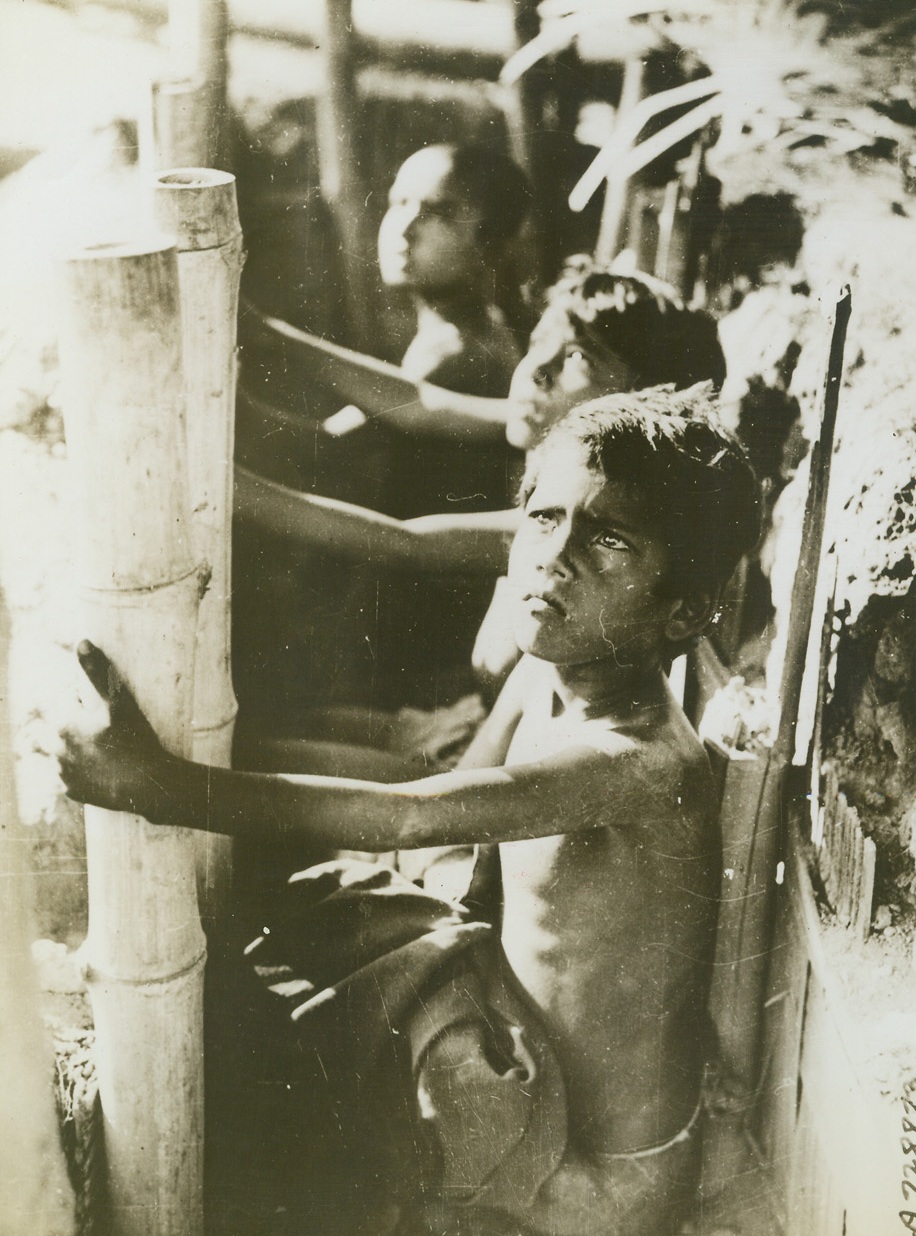 Fearful Eyes of the Innocent, 6/30/1944. Bengal—Fear grips the faces of these Bangal children as they sit in slit trenches and anxiously watch strafing Jap zeros pass overhead. Children like these the world over have never know the wonders of peace being born into maddened civilization brought on by the tyranny of the axis.  Bamboo poles and basketwork support the sides of the trench offering the native youngsters protection.Credit (British official photo from ACME);