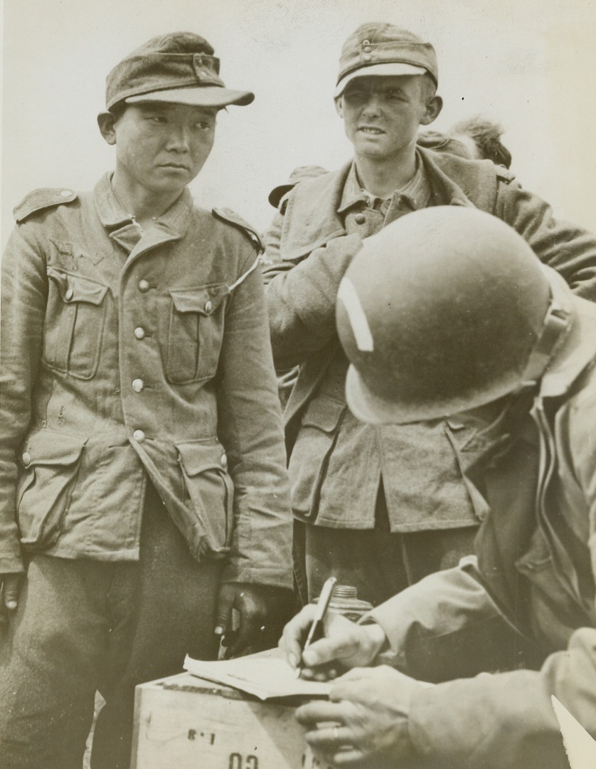 Captured Jap in Nazi Uniform, 6/21/1944. France – Fearful of his future, this young Jap, wearing a Nazi uniform, is checked off in a roundup of German prisoners on the beaches of France. An American Army Captain takes the Jap’s name and serial number. Credit: Coast Guard Photo from ACME;