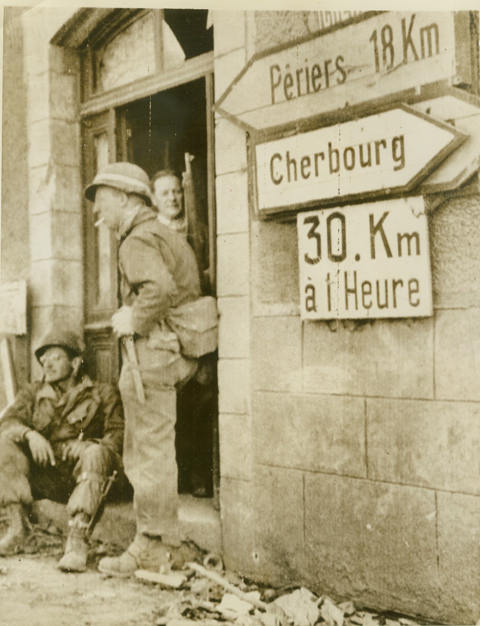 Speed Limit-Unlimited, 6/19/1944. France—Yank troops pushing steadily toward Cherbourg rest beside a sign pointing to that important port. Speed limit is posted at 30 kilometers an hour (approximately 18 miles) but that doesn’t apply to Allied soldiers who have now isolated an estimated 30,000 enemy troops in Cherbourg. Credit: Signal Corps radiotelephoto from ACME;