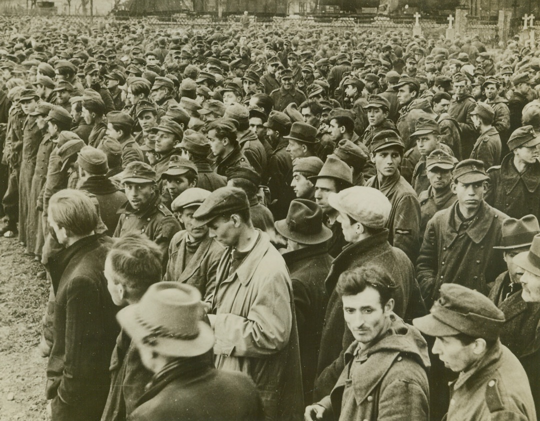 De-armed Army, 3/30/1945. Germany—Droves of German prisoners, captured as the American forces advanced across the Rhine at Remagen, are packed into this area to await transfer to prison camps. Note some in civilian clothes. They deserted from the German army and hid in cellars and other hide-outs until American forces reached them. Prisoners, which daily number in the thousands, are rapidly swelling the Allied prison camps to capacity. Credit: ACME.;
